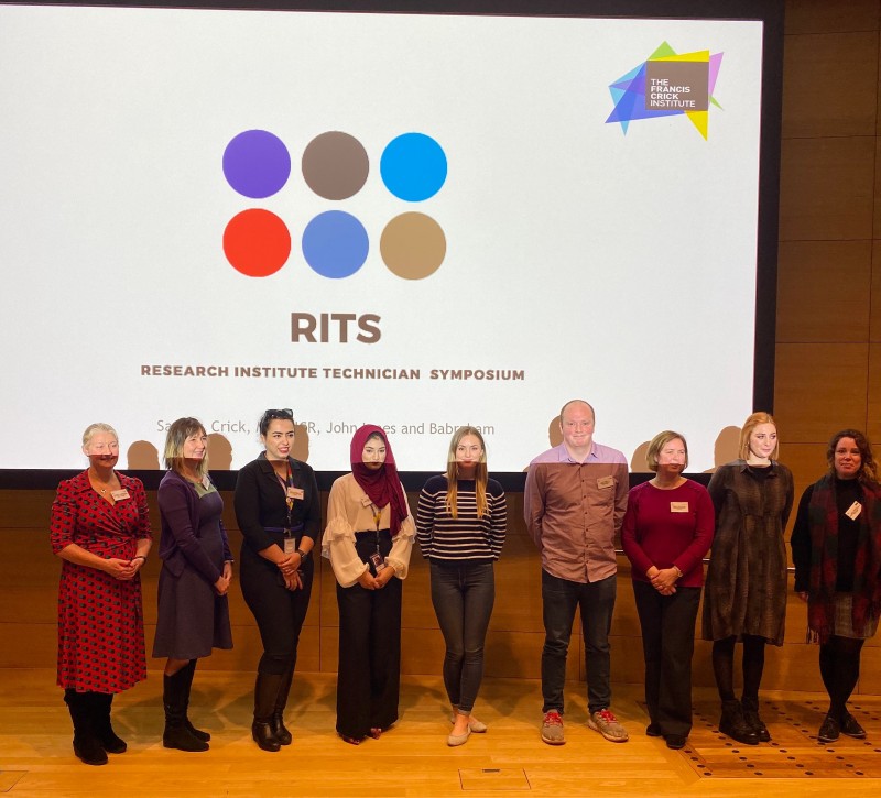 Group stood in front of RITS (Research Institute Technician Symposium) logo